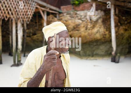 shepard africano invecchiato camminando sulla spiaggia tenendo bastone Foto Stock