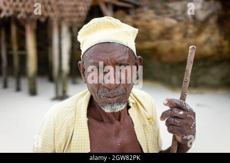 shepard africano invecchiato camminando sulla spiaggia tenendo bastone Foto Stock