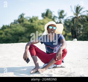 Uomo africano seduto sulla spiaggia di sabbia Foto Stock