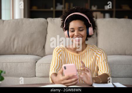 Felice giovane donna africana in cuffie utilizzando cellulare. Foto Stock