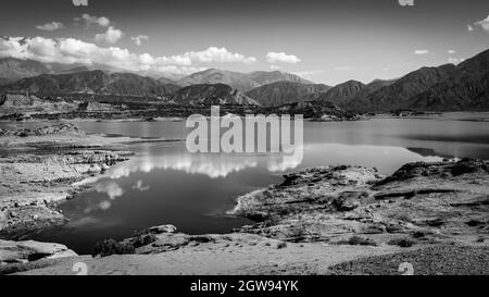 Una foto in scala di grigi di un lago circondato da montagne in una zona rurale Foto Stock