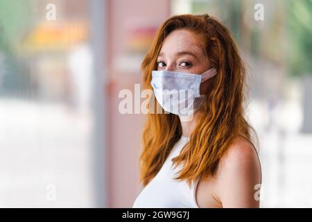 Giovane donna dai capelli rossi con maschera chirurgica, protezione e precauzione per le malattie contagiose. Interruzione del virus Corona. Foto di alta qualità Foto Stock