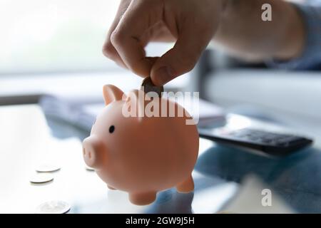 Raccolto primo piano uomo mettendo moneta in rosa Piggy banca Foto Stock