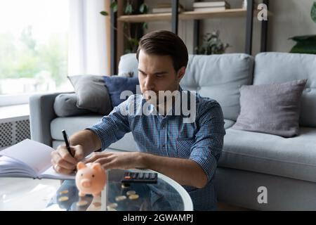 Uomo serio che gestisce le finanze, seduto a tavola con la banca Piggy Foto Stock