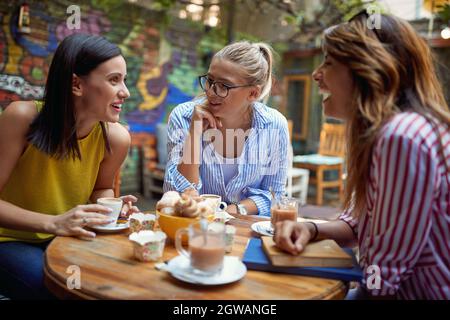 gruppo di giovani amici caucasici adulti che parlano e ridono in un bar all'aperto, bevendo caffè. concetto di gossip Foto Stock