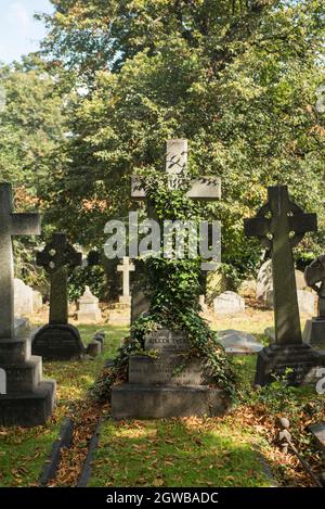 Un monumento crociato sopraffolto di edera tra le lapidi in un cimitero vittoriano a Londra, Regno Unito. Foto Stock