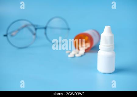 primo piano della bottiglia di goccia dell'occhio e dell'occhiale su sfondo blu , Foto Stock