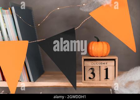 Buon calendario di Halloween in legno con la data 31 ottobre sulla libreria. Zucca sul calendario. Bandiere nero arancione decorazioni di festa. Foto Stock