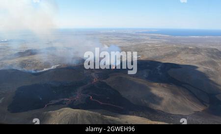 Il campo di lava a Fagradalfjall, Islanda. Bocca attiva con eruzione di lava fusa e aumento di gas vulcanico. Lava nera e cielo blu. Immagine aerea. Foto Stock