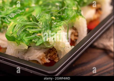 Delizioso sushi roll con formaggio Philadelphia, cetriolo, salmone e chuka in un vassoio di plastica su un tavolo di legno Foto Stock