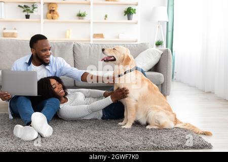 Vita domestica. Ritratto di coppia felice trascorrere il tempo insieme a casa in soggiorno, ragazzo utilizzando il computer e stroking labrador, donna sdraiata su boyfri Foto Stock