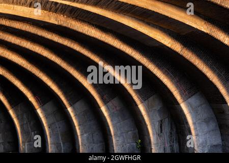 Linee astratte a contrasto, curve e illuminate al sole, sotto il vecchio ponte ferroviario al tramonto, struttura in pietra e mattoni ad arco, gioco di luci e ombre a Berlino, Germ Foto Stock