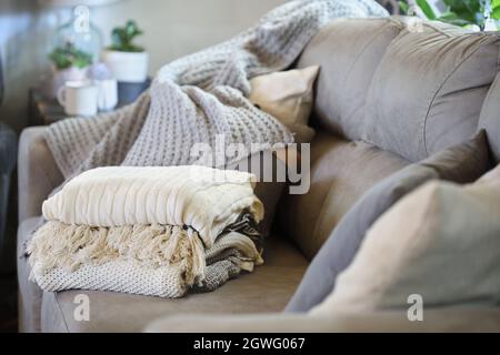 Pila di una varietà di coperte di tiro a maglia morbida impilata su un divano in un soggiorno stile fattoria. Messa a fuoco selettiva primo piano e sfondo sfocati. Foto Stock