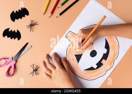 primo piano delle mani dei bambini che dipingendo la zucca con il viso spoky Foto Stock