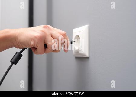 La mano donna inserisce una spina elettrica nel primo piano della presa Foto Stock