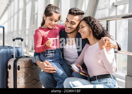 Felice genitori arabi con carino figlia in attesa di volo in aeroporto Terminal, Medio Oriente Famiglia di tre che viaggiano insieme all'estero, Femminile Foto Stock