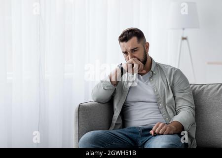 Infelice depresso maschio caucasico seduta, piangendo in soggiorno, sentendosi disperato, solo, in stressato dal lavoro, perso, disoccupazione e ansia. Triste Foto Stock