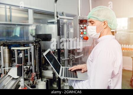 ingegnere che lavora con il computer portatile in un ispettore per la produzione di macchine alimentari con indumenti igienici. Foto Stock