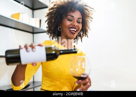 Una donna africana sorridente versa il vino nel calice Foto Stock