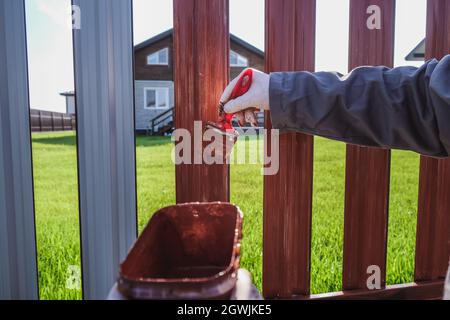 Un uomo dipinge una recinzione in ferro nel giardino Foto Stock