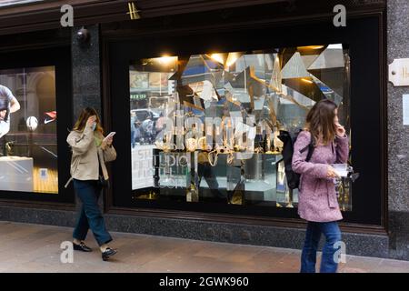 Knightsbridge, Londra, Gran Bretagna. 30 Settembre 2021. Donna che indossa una copertura del viso controllando il suo telefono cellulare mentre lei cammina oltre la vetrina del negozio Foto Stock