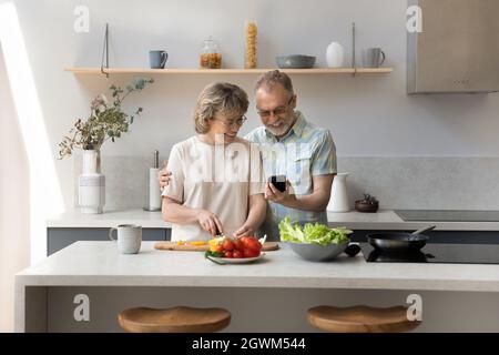 Felice affettuoso medio invecchiato coppia web surf ricetta in cellulare. Foto Stock