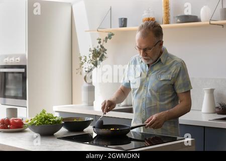 Buon uomo di mezza età che cucina cibo in cucina. Foto Stock