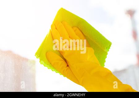 con la mano un guanto di gomma giallo si pulisce il vetro in primo piano Foto Stock