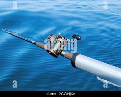 Canna da pesca con mulinello in acqua di lago blu Foto Stock