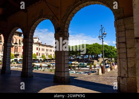 Desenzano del Garda, Italia - 22 settembre 2021: Vista sul porticciolo del lago attraverso il portico della piazza. Foto Stock