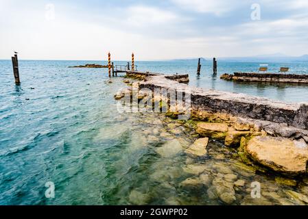 Tranquilla riva del Lago di Garda in una giornata piovosa vicino al molo vuoto. Foto Stock