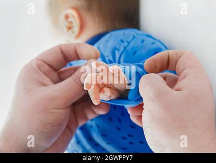 Le mani del papà si arrotolano sulle maniche della mano del bambino, in primo piano. Neonato in ospedale, amore e cura del padre del genitore. Foto Stock