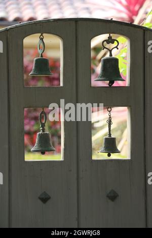 Bella porta in legno di vecchio stile spagnolo con quattro campane d'epoca pendenti in metallo. Foto Stock