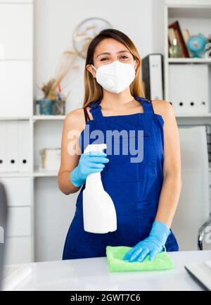 Donna ufficio pulitore in maschera Foto Stock