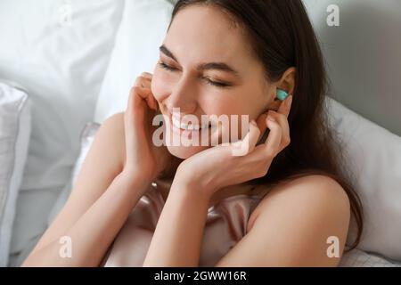 Bella giovane donna mettere tappo auricolare prima di dormire in camera da letto, primo piano Foto Stock