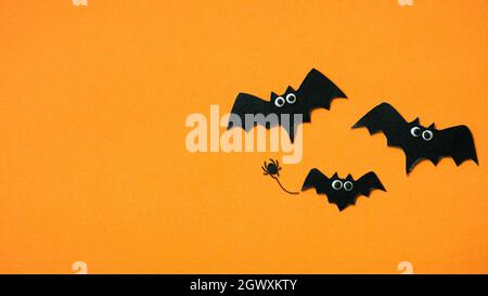 Tema di Halloween con pipistrelli divertenti, piatto. Vista dall'alto delle decorazioni della famiglia dei pipistrelli su sfondo arancione con spazio per il testo Hallowen. Buon Halloween, divertimento Foto Stock