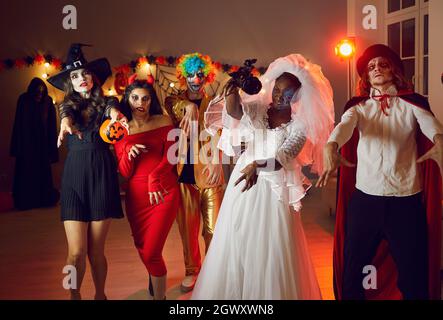 Gruppo di persone adulte in costumi spooky che camminano come zombie al partito di Halloween Foto Stock