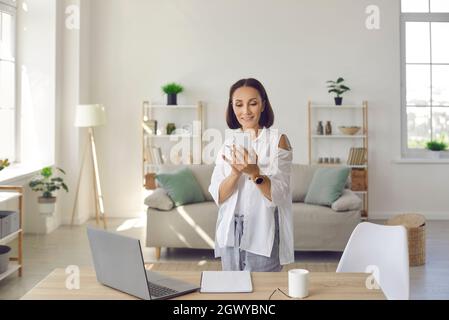 Ritratto di elegante donna anziana in piedi con telefono vicino al posto di lavoro nel suo ufficio domestico. Foto Stock