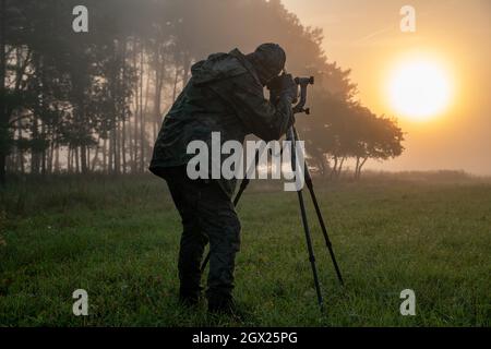 Fotografo della natura in piedi in abiti camuffati con una macchina fotografica su un cavalletto Foto Stock