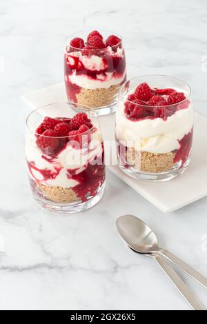 Tre bicchieri riempiti con dessert di cheesecake al lampone senza cottura su sfondo di marmo bianco con spazio copia. Vista angolata. Foto Stock