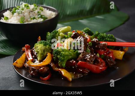 Manzo teriyaki asiatico con peperoni rossi e gialli, broccoli e semi di sesamo su un piatto sul tavolo. Manzo teriyaki piccante friggere con le verdure Foto Stock