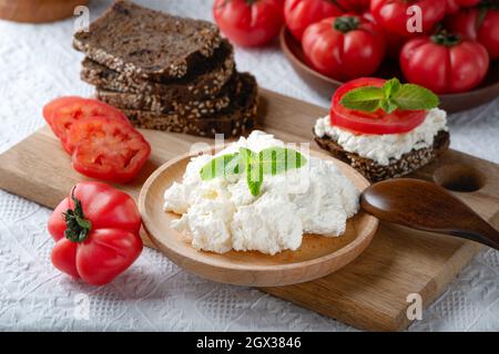 Fette di pane di segale con formaggio casereccio e pomodori su piatto di legno Foto Stock