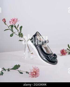 Scarpe nuove ed eleganti per la scuola per una ragazza in una composizione di fiori su sfondo bianco Foto Stock