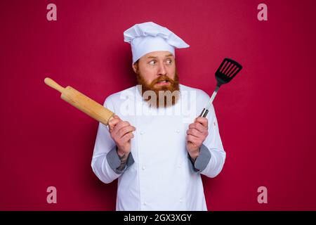 lo chef dupter con barba e grembiule rosso tiene la spilla in legno Foto Stock