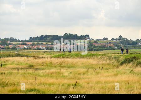 Camminatori sul sentiero circolare Blakeney Freshes con Blakeney villaggio sullo sfondo. Norfolk, Inghilterra. Foto Stock