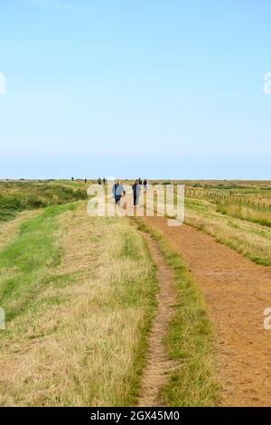 Persone che camminano sul sentiero Blakeney Freshes con una vista ampia sulle paludi. Norfolk, Inghilterra. Foto Stock