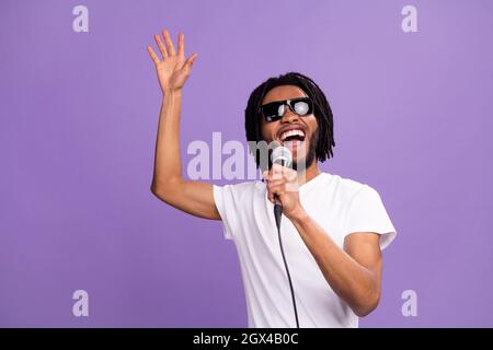 Foto di allegro giovane afro americano funky uomo cantare karaoke indossare occhiali da sole isolato su sfondo di colore viola Foto Stock