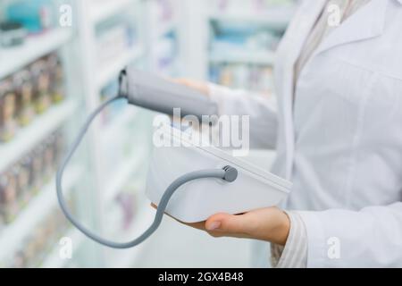 vista croppata del farmacista in cappotto bianco che tiene tonometro digitale in farmacia Foto Stock