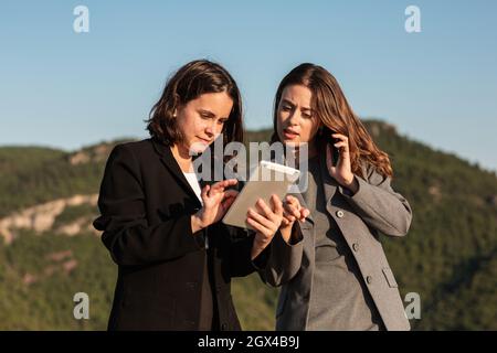 Donne d'affari focalizzate che lavorano insieme su tablet e smartphone Foto Stock