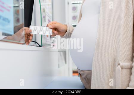 vista croppata del farmacista che dà il blister con il farmaco alla donna incinta al banco Foto Stock